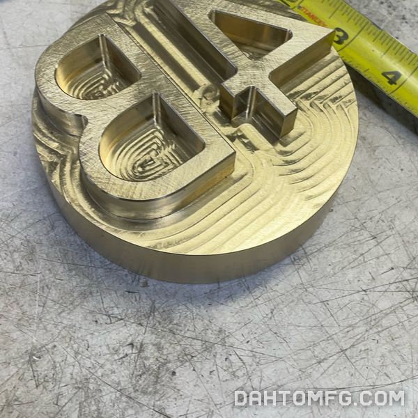 Round brass part with a raised 84, with a tape measure for scale