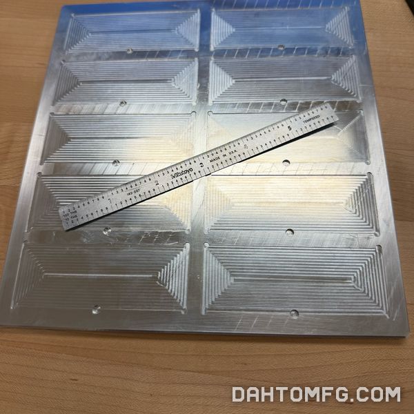 Aluminum plate with ten machined pockets and a steel rule for scale